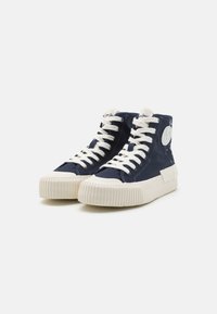 Navy canvas high-top sneakers with white rubber sole, round toe, and beige laces. Features logo patch on the side and textured panels.