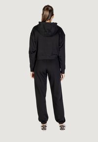 Haut de survêtement noir coupé avec une capuche, accompagné de joggings noirs assortis. Les joggings possèdent des poignets élastiqués, et l'ensemble est complété par des baskets à motifs.
