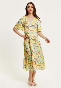 Maxi dress in yellow fabric featuring a colorful abstract pattern with blue, pink, and brown. V-neckline, short flutter sleeves, tiered design.