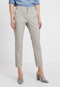 Pantalon beige clair sur mesure avec une coupe décontractée et des ourlets poignets, en tissu mélangé coton ; associé à des mules à talons gris à imprimé serpent.