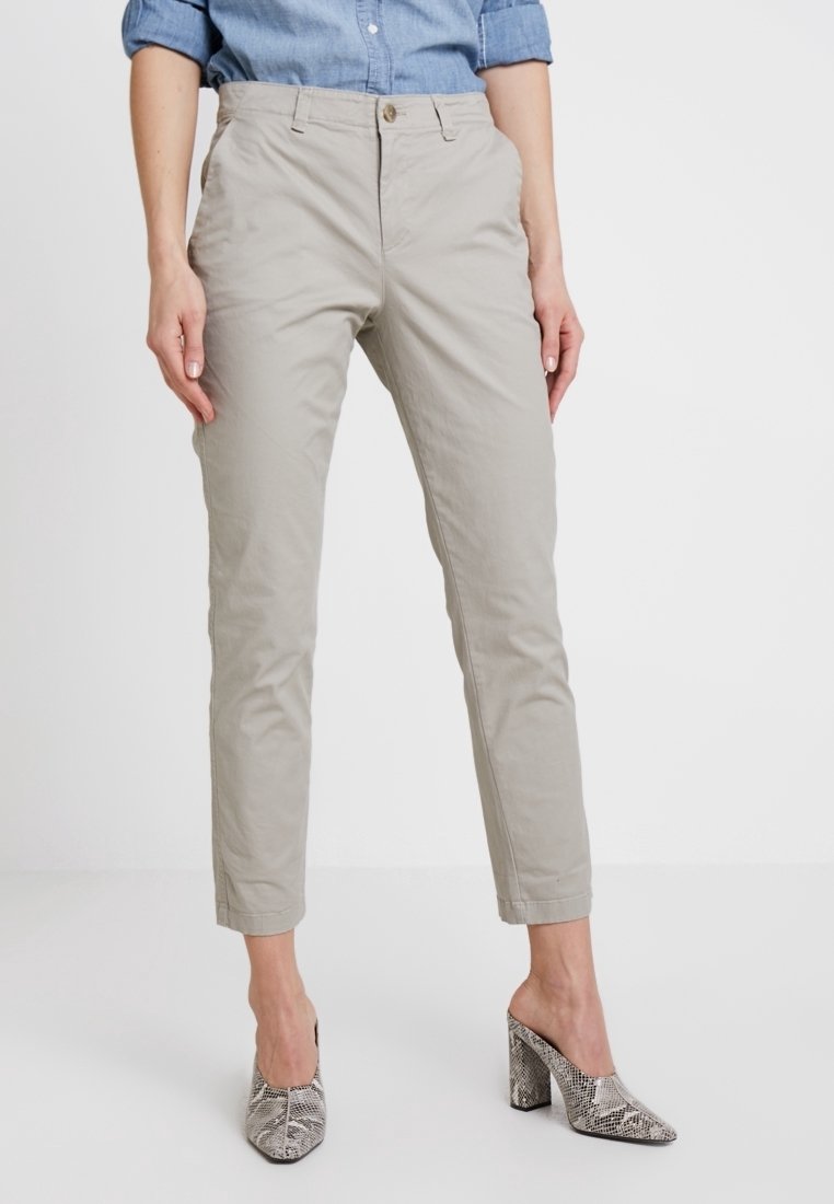 Pantalon beige clair sur mesure avec une coupe décontractée et des ourlets poignets, en tissu mélangé coton ; associé à des mules à talons gris à imprimé serpent.