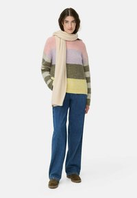 Mehrfarbiger Strickpullover mit Streifen in Pink, Lavendel, Grün und Gelb, kombiniert mit blauen weit geschnittenen Jeans und einem cremefarbenen Schal.