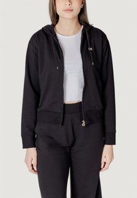 Felpa nera con zip realizzata in morbido tessuto, con un design cropped, caratterizzata da una chiusura frontale con zip, tasche laterali e una vestibilità rilassata.