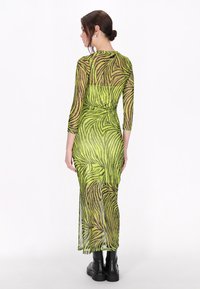 Rochie verde transparentă cu un model de dungi zebra, având mâneci lungi și o siluetă ajustată, asortată cu cizme negre până la glezne.