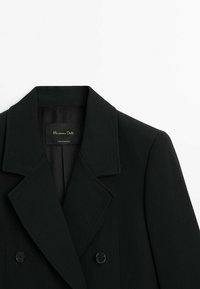 Blazer noir croisé avec larges revers et deux boutons visibles, montrant l'étiquette intérieure "Massimo Dutti Made in Portugal."