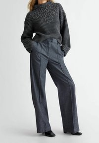 Ciemnoszary sweter wykonany na drutach z teksturowanym kwiatowym wzorem przy dekolcie, zestawiony z ciemnoszarymi spodniami o wysokim stanie i szerokimi nogawkami oraz czarnymi butami.