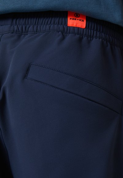 Marineblaues Hosen aus glattem Stoff mit elastischem Bund. Mit einer flachen Gesäßtasche und einem orangefarbenen Markenetikett mit der Aufschrift "FIRE+ICE".