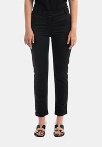 Pantaloni neri aderenti con passanti per cintura, tasche frontali e risvolti, realizzati in tessuto twill. Abbinati a sandali piatti a ciabatta.