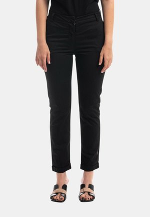 Pantaloni neri aderenti con passanti per cintura, tasche frontali e risvolti, realizzati in tessuto twill. Abbinati a sandali piatti a ciabatta.