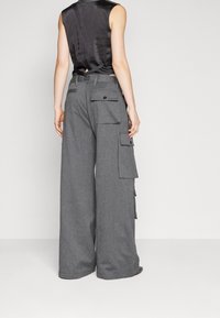 Szare szerokie spodnie cargo z teksturowanej tkaniny, z bocznymi i tylnymi kieszeniami oraz luźnym krojem. Widok z tyłu pokazuje regulowany pas.