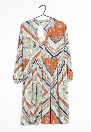 Pitkähihainen V-kaula-aukollinen mekko, jossa vihreitä, oransseja, valkoisia ja mustia paisley-kuvioita ja geometrisiä kuvioita, ripustettuna mustalle henkarille.