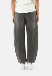 Pantaloni in denim grigio a gamba larga con una finitura sbiadita, dotati di due tasche posteriori, orlo dritto e una texture del tessuto usurata. Abbinati a sneaker bianche.