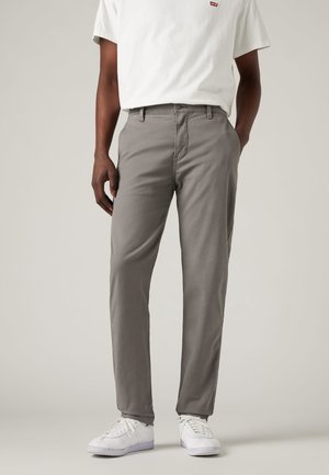 Pantalons en coton gris avec une coupe droite. Comprend des passants de ceinture, des poches avant et une fermeture à bouton. Portés avec des baskets blanches.