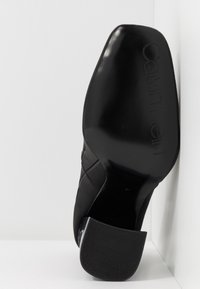 Černá lodička na vysokém podpatku s hladkým, lesklým povrchem; na podrážce je vyražené logo "Calvin Klein"; má strukturovanou úpravu pro lepší protiskluz na podpatku.