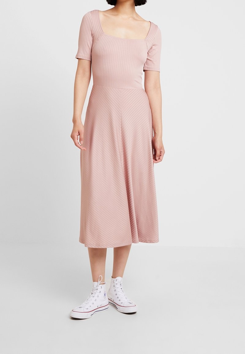 Robe midi côtelée rose avec un col carré et des manches courtes, associée à des baskets montantes blanches. Texture lisse et rayures subtiles.
