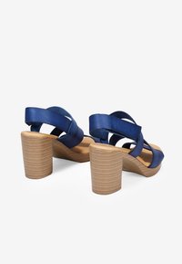Sandalias de tacón azul marino con tiras entrecruzadas, tacones de bloque de madera y un acabado suave. Forro suave y diseño de puntera redondeada.