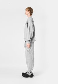 Sudadera gris y pantalones a juego hechos de un tejido suave, con un corte holgado, puños acanalados y un detalle de cadena en los pantalones. Combinados con calzado negro.
