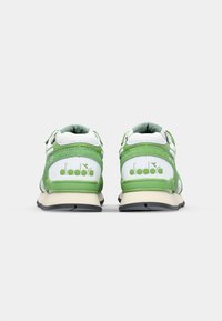 Green and white athletic shoes with a textured upper, padded collar, and black rubber outsole. Logo prominently displayed on the heel.