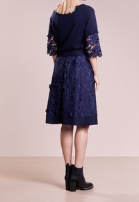 Topp jordblått strikket stoff med dekorative blondeermer, kombinert med et matchende blondeskjørt. Skjørtet har en rynket midje og en ensfarget kant. Svarte ankelstøvler.