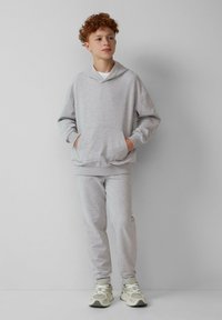 Lichtgrijze hoodie met een voorzak en bijpassende joggingbroek. Zachte stof, relaxte pasvorm en ribgebreide boorden. Draagt met crèmekleurige sneakers.