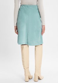 Een muntgroene corduroy rok met een rechte snit, achterboord en soepele textuur, gecombineerd met beige kniehoge hakken.