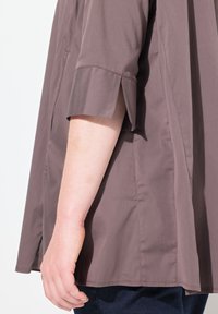 Top corto marrone a maniche corte con un design a polsino aperto, tessuto leggero e vestibilità comoda, abbinato a denim scuro in vita.