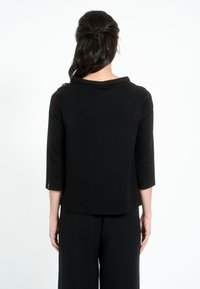 Črna majica s tremi četrtinami rokavi in širokim ovratnikom, narejena iz gladkega materiala, s subtilnimi šivi in preprostim dizajnom na hrbtni strani.