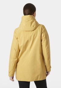 Chaqueta impermeable amarilla con capucha, con mangas largas, corte recto y textura suave, mostrada desde atrás.