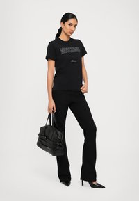 Melnā t-kreklā ir uzdrukāts teksts "Moschino Milano" sudraba krāsā. Kombinēts ar melnām platām biksēm un melnu rokassomu. Augstpapēžu melnas kurpes.