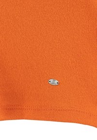 Tessuto lavorato a maglia arancione con una consistenza liscia, caratterizzato da una piccola etichetta argentata stampata con "KEY LARGO" vicino al bordo inferiore.