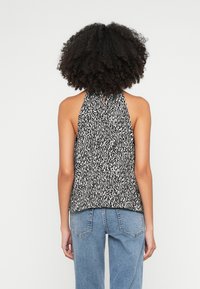 Melns un balts haltera topi ar abstraktu rakstu, vieglu audumu un aizdari ar saiti aizmugurē. Saskaņots ar gaismas ziliem džinsiem ar augstu jostasvietu.