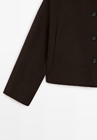 Giacca buttonata marrone scuro con maniche lunghe e una tasca verticale sul davanti, su sfondo bianco.