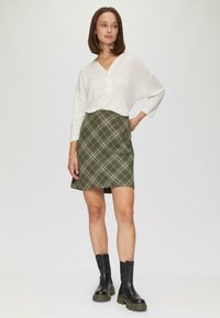 Biała, luźna bluzka z dekoltem w serek połączona z zieloną, kratkowaną mini spódnicą. Czarne botki za kostkę z grubą podeszwą dopełniają strój.