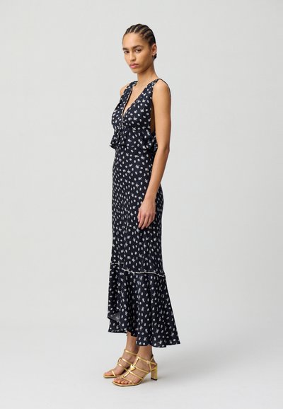 Vestido floral navy con escote con volantes, cuerpo ajustado y dobladillo acampanado. Combinado con sandalias doradas de tacón con tiras. Textura de tela suave.