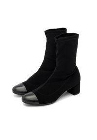 O pereche de botine negre până la jumătatea gambei, cu toc pătrat și vârfuri din piele netedă, realizate dintr-un material elastic care se mulează pe glezne.