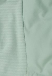 Licht mintgroen stof met twee texturen: links een geribbeld patroon, rechts een gladde, licht glanzende oppervlakte.