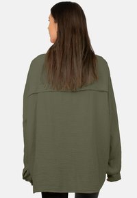 Overmaatse olijfgroene shirt van textuurstof, met een brede snit, lange mouwen en een horizontale naad op de rug.