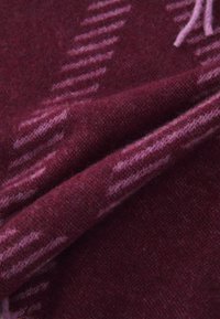 Tecido de lã burgundy com uma textura suave, apresentando riscas diagonais em rosa e padrões alternados, dobrado para exibir profundidade e detalhe.