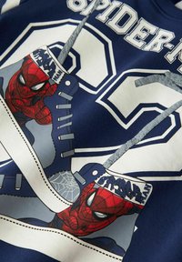 Sweatshirt bleu marine avec un motif Spider-Man accentué de rouge, grand "23" blanc sur la poitrine et des lacets et textures gris.