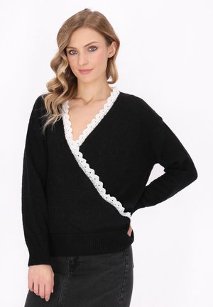 Black sweater with a deep V-neck, trimmed with white scalloped lace. Loose fit, long sleeves, and ribbed cuffs. Paired with a dark skirt.