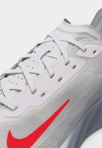 Κοντινή λήψη λευκού και γκρι παπουτσιού Nike για τρέξιμο με λευκά κορδόνια και φωτεινό κόκκινο λογότυπο Nike σε υφασμάτινο, υφή ανώτερο μέρος.