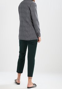 Harmaa ruudullinen bleiseri, jossa on räätälöity istuvuus, yhdistetty tummanvihreisiin lyhytlahkeisiin housuihin. Asua täydentävät matalat liukuvillaset kengät, joissa on rusetti.