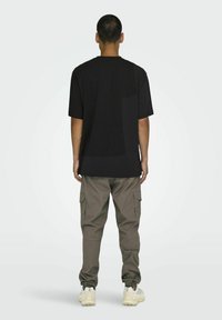 Svart kortärmad t-shirt med en stor central bakpanel; i kombination med kaki cargobyxor med sidofickor och elastiska ärmslut.