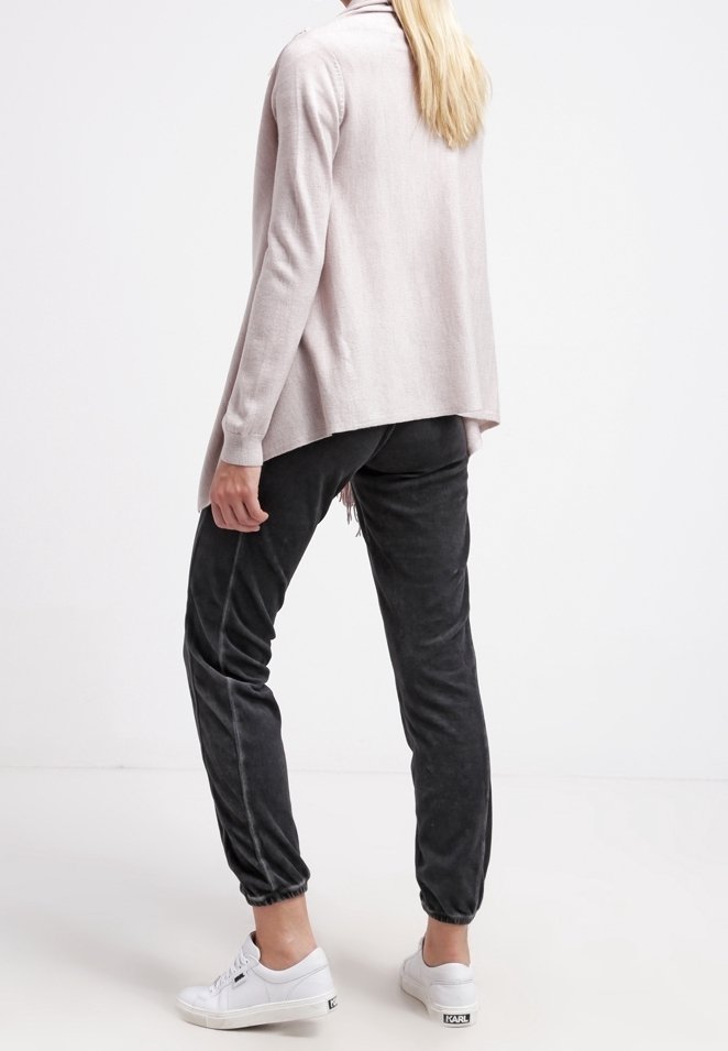 Hellrosa Langarmshirt, weicher Stoff, lockere Passform, kombiniert mit dunkelgrauen, taillierten Hosen, elastischen Bündchen und weißen Sneakers.