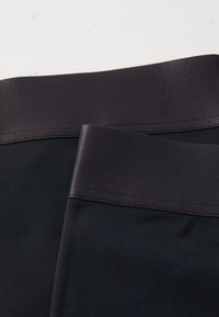 Svarta leggings med en slät, elastisk yta, med ett kontrasterande mörkt midjeband och snygg sömnad längs kanterna.