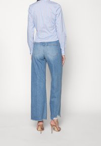 Camicia a maniche lunghe a righe azzurre abbinate a jeans in denim azzurro a gamba larga. Le scarpe con i tacchi sono beige e i jeans presentano dettagli strappati sull'orlo.