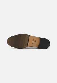 Black leather shoe sole with a smooth texture and horizontal grooves. Features a tan insole with printed branding and size details.