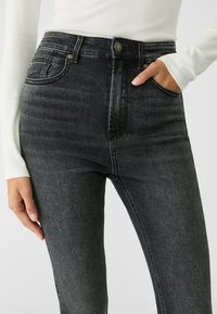 Höga svarta denimjeans med en slät yta, fem fickor och subtila blekningar på framsidan. Knapp- och dragkedjes stängning vid midjan.