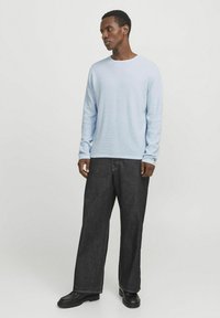 Suéter de punto azul claro con mangas largas y cuello redondo; combinado con pantalones de mezclilla oscuros y holgados y botas negras. Textura y diseño simples.