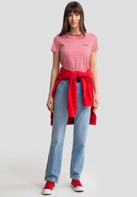 Červené a bílé pruhované tričko, červená mikina uvázaná v pase, světle modré džíny a červené tenisky. Jednoduchý, ležérní outfit.